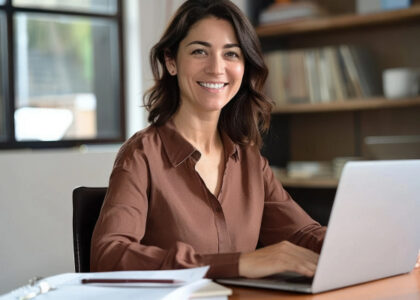 Tax professional smiling while working on a laptop at a desk in a bright office.