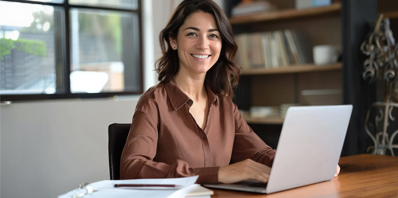 Tax professional smiling while working on a laptop at a desk in a bright office.