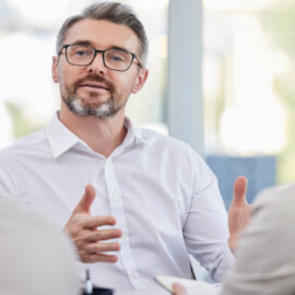 Tax professional explaining small business tax guidance to two clients in a bright office meeting.