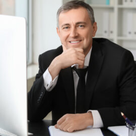 Tax professional smiling while working at a home office desk with a computer and paperwork.