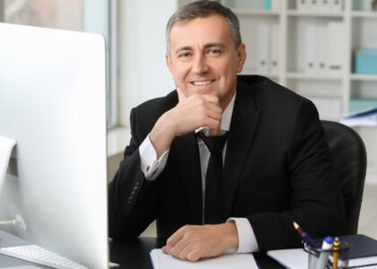 Tax professional smiling while working at a home office desk with a computer and paperwork.
