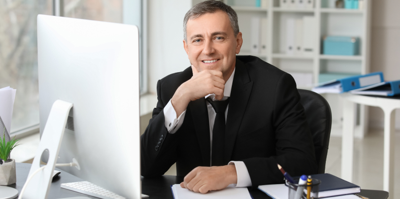 Tax professional smiling while working at a home office desk with a computer and paperwork.
